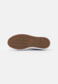 Semelle de sneaker en caoutchouc blanc avec une semelle d'adhérence texturée marron, présentant des motifs géométriques et des détails de branding. Bords lisses et design arrondi.