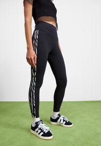Black leggings with a high waistband, featuring a white zebra stripe pattern along the sides, paired with dark sneakers and white socks.