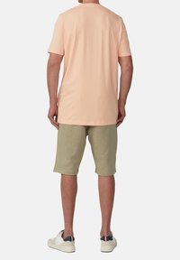 Hellbeige Baumwoll-T-Shirt mit kurzen Ärmeln, kombiniert mit olivgrünen Shorts. Das Outfit wird mit weißen Sneakers mit schwarzen und roten Akzenten abgerundet.