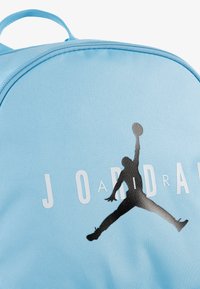 Light blue fabric backpack featuring a large black graphic of a jumping figure, with the word "JORDAN" partially visible below.