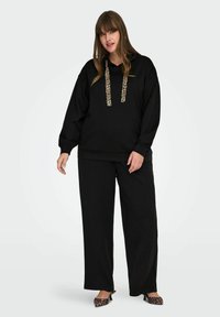 Juodas gobtuvas su gyvūnų rašto virvutėmis, derinamas su laisvomis juodomis kelnėmis ir leopardų rašto butais. Minkšta medžiaga ir laisvas siluetas.