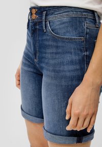 Jeansowe szorty w ciemnym odcieniu z zapięciem na dwa guziki, dopasowany krój, podwinięte rękawy oraz subtelne przetarcia z przodu.