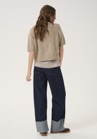 Beige kortærmet strikket sweater lagdelt over en stribet langærmet skjorte, parret med bredbenede mørke denim jeans med rå kant og manchetter.