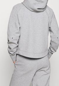 Grå sweatshirt med huva, ribbad muddar och nederkant. Tillverkad av mjukt material, har raglanärmar och en något kortad bakdesign.