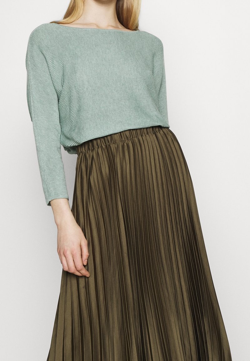 Light green ribbed knit sweater paired with a pleated, high-waisted olive brown skirt. The skirt has a soft, flowing texture.