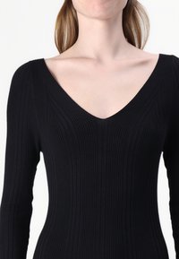 Black ribbed long-sleeve top with a deep V-neckline. The fabric is textured, featuring vertical ribbing for added visual interest.