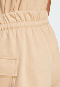 Beige joggingové kalhoty s nařaseným elastickým pasem a boční kapsou, vyrobené z měkké, texturované tkaniny.