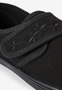 Chaussure noire en toile avec une bande Velcro, broderie florale décorative et tige texturée, dotée d'une semelle en caoutchouc contrastée.