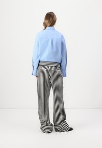 Light blue collared shirt, long sleeves, and black-and-white striped wide-leg pants with cuffs. Fabric appears smooth and breathable.