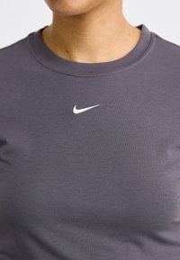 Grijze katoenen t-shirt met een ronde halslijn, voorzien van een klein wit Nike-logo op de bovenste linkerkant van de borst. Gladde textuur, korte mouwen.