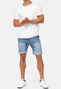 Witte korte mouwen t-shirt gecombineerd met opgerolde blauwe denim short en witte sneakers. De outfit is casual en eenvoudig van ontwerp.