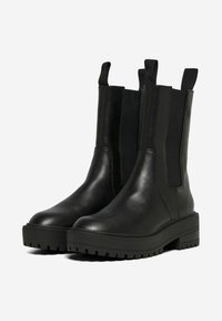 Bottines en cuir noir avec des panneaux latéraux élastiques, des bouts arrondis et des semelles en caoutchouc texturé avec des rainures profondes.