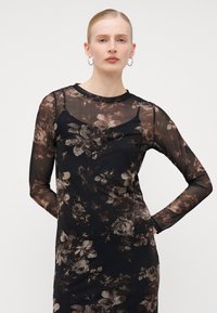 Robe noire à motifs floraux avec de longues manches transparentes, présentant un tissu texturé et un col rond. Motif floral dans des tons de marron et de gris.