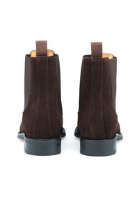 Bottines en suédine marron avec des panneaux latéraux élastiques, un talon renforcé et une semelle noire texturée. Le design comprend une languette pour un enfilage facile.