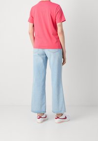 Camiseta de algodón rosa combinada con jeans de pierna ancha de un azul claro y zapatillas blancas con detalles en rojo. Diseño sencillo con un ajuste relajado.