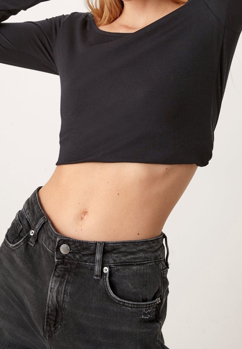 Svart beskuren långärmad topp i kombination med högmidjade grå jeans med slitningar, silverdetaljer och en mjuk yta.