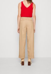 Pantalons larges beiges à taille haute, avec des poches arrière et une finition soignée. Associés à un top rouge sans manches et des chaussures à talons beiges.