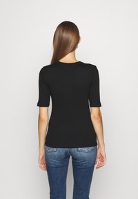 Svart ribbad t-shirts med korta ärmar, rundad hals, figurnära passform. Bärs med blå denimjeans, visas bakifrån.