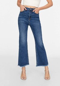 Jean évasé taille haute en denim bleu foncé avec un ourlet brut, doté de poches avant et d'une fermeture à boutons dissimulée.