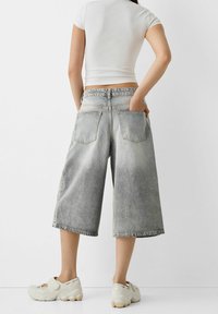 Culottes en denim gris délavé avec une coupe décontractée, dotées de deux poches arrière et d'un ourlet effiloché, accompagnées de chaussures de sport de couleur claire.