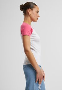T-shirt blanc à manches courtes avec des manches raglan roses, design ajusté, en coton lisse, porté avec une jupe en denim bleu clair présentant des effets de déchirure.