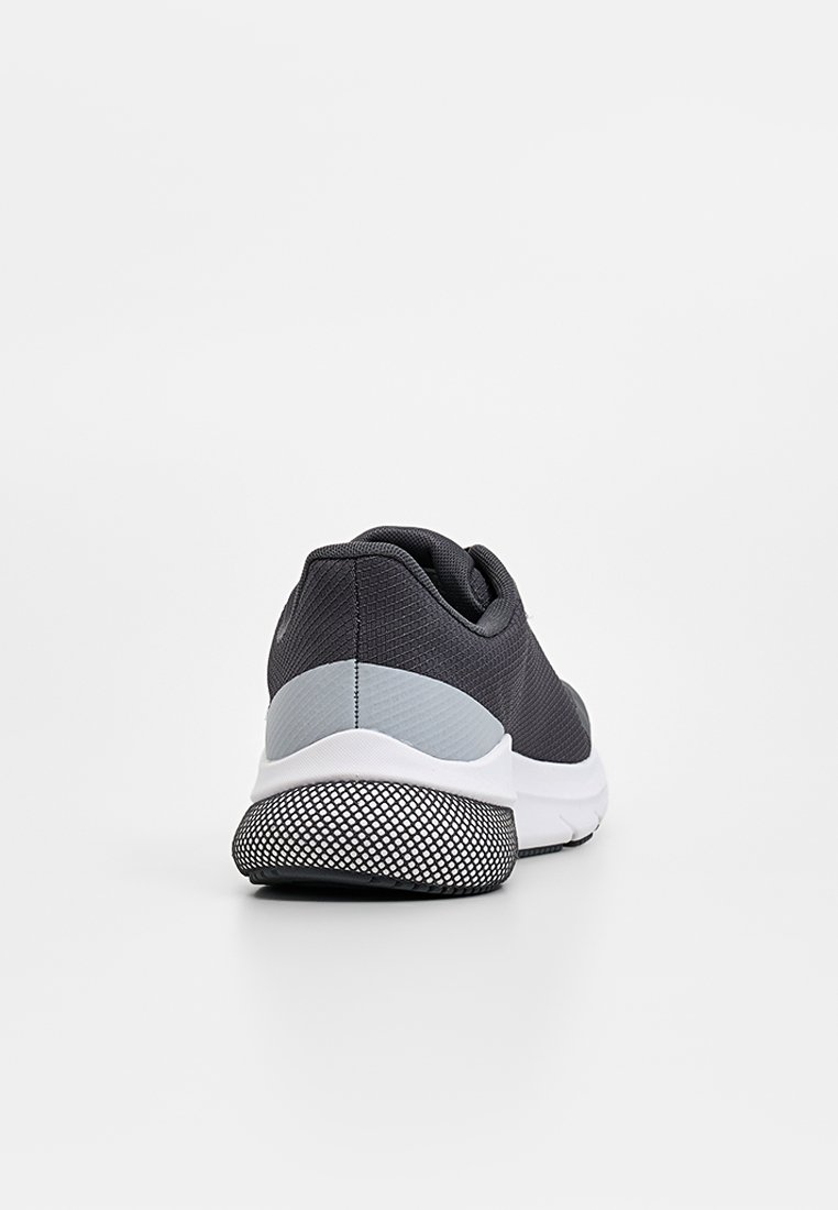 Zapatilla deportiva de color gris oscuro con un empeine texturizado, un acento en el talón de color gris claro y una suela blanca con un patrón negro de puntos.