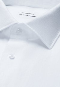 Col de chemise blanche avec deux boutons transparents et une étiquette de marque « seidensticker » cousue à l'intérieur de l'encolure.