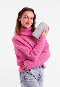 Pink knitted sweater with a high collar, loose fit, and ribbed texture. The model holds a gray wallet with a subtle pattern and logo.