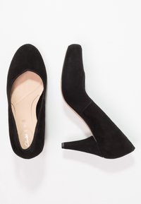 Des escarpins en suède noir à talons avec un bout rond et une doublure intérieure lisse. Les talons mesurent environ 3 pouces de haut et présentent des coutures minimales.