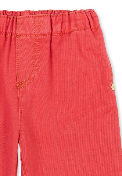 Pantaloni di colore corallo con fascia elastica in vita, tasca laterale funzionale e cuciture arancioni visibili.