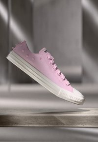 Rosa lerret sneakers med hvit gummisåle, rund tå og snøring. Har hevede prikker og pigger langs siden for detaljer.
