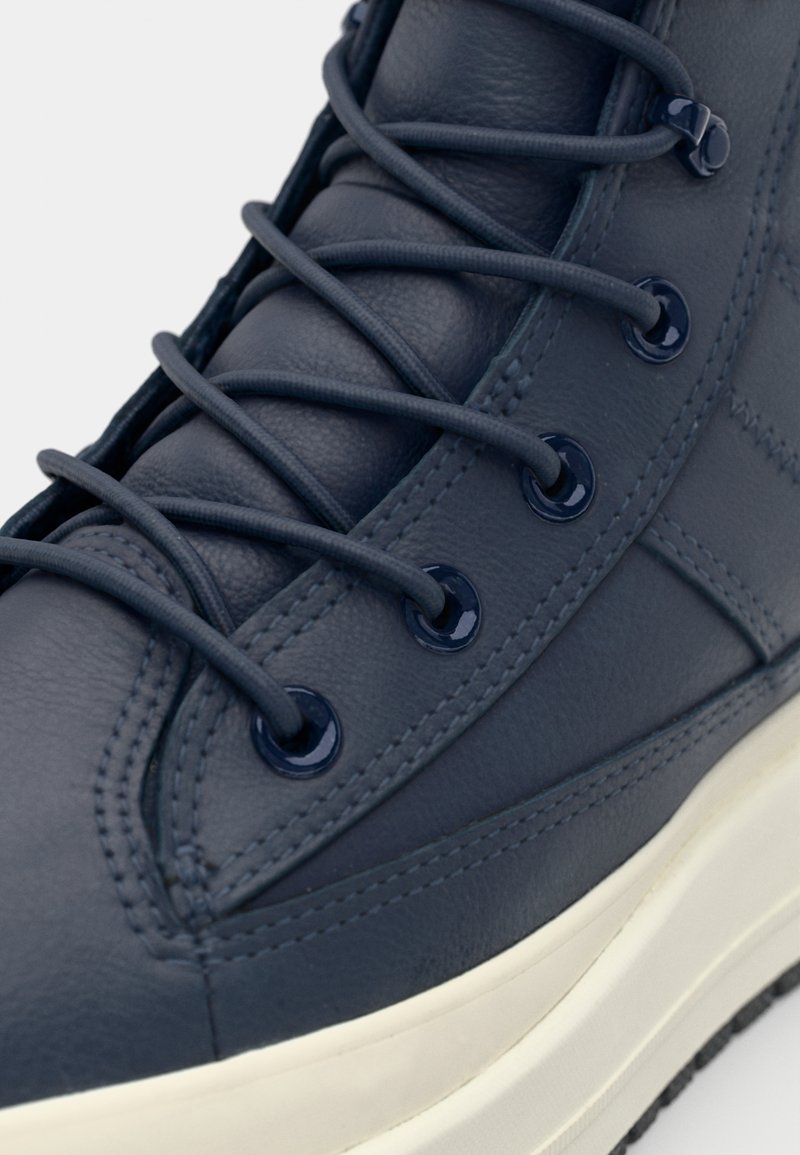 Mörknavy läder hög topp sneakers med rund tå, tonade snören och glänsande öglor, med en vit gummisula och synlig sömnad.