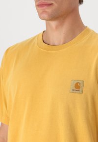 T-shirt in cotone giallo con scollatura tonda, dotata di un logo a patch quadrato sull'area sinistra del petto. Tessuto morbido e vestibilità regolare.