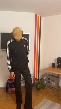 Veste zippée noire Adidas avec des rayures blanches, assortie à un pantalon noir et une casquette beige. Présente un design minimaliste et une texture lisse.