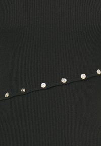 Tissu côtelé noir avec une rangée diagonale de petits boutons décoratifs ronds argentés et dorés.