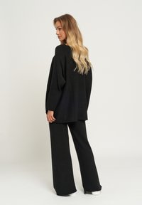 Czarny, dzianinowy, oversize'owy top z opadającymi ramionami, dopasowany do szerokich spodni. Gładka tekstura i luźny fason. Prosty design.
