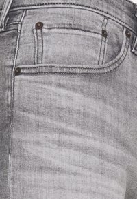 Grijze denim jeans met een licht vervaagd textuur, voorzien van gestikte naden, twee voorzakken en koperen accenten.