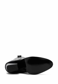 Scarpa nera in pelle con un design elegante, caratterizzata da una punta affilata e una suola curva e liscia. Include un tacco basso e dettagli minimi.