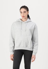 Gray hoodie in soft, textured fabric with a front pocket, drawstrings on the hood, and ribbed cuffs. Worn with black pants.