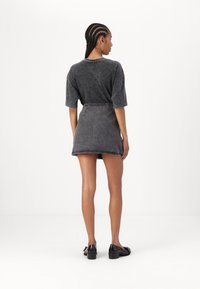 Grå denimminikjol kombinerad med en matchande oversized grå t-shirt. Har en avslappnad passform och subtila sömdetaljer. Svarta skor fulländar looken.