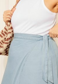 Világoskék, puha anyagból készült, kötött derékpántos, oldalhasítékos szoknya. Kézzel szőtt táska tejszínes és rozsdabarna csíkos mintával.