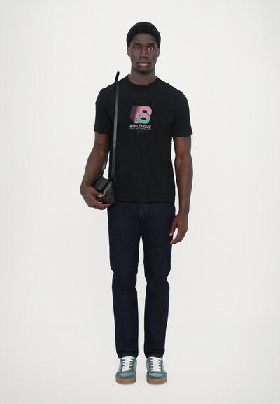 Black t-shirt with colorful graphic, blue jeans, and green sneakers. Accessories include a small black crossbody bag.