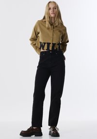 Camisa beige de botonadura corta con la palabra "WILD" en letras negras, combinada con jeans negros de cintura alta y zapatos de plataforma marrones con cordones.