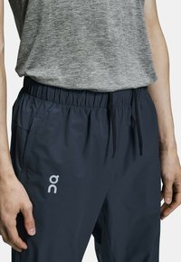 Tmavě modré sportovní kalhoty s elastickým pasem a šňůrkou. Obsahují boční kapsu a reflexní logo na levém stehně.