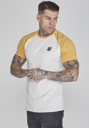 White and yellow raglan t-shirt with short sleeves, featuring a small black logo on the chest. Fabric appears smooth, with a lightweight design.