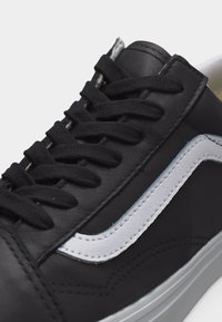 Baskets en cuir noir avec des lacets noirs, une bande latérale blanche et une semelle blanche, présentées en gros plan.