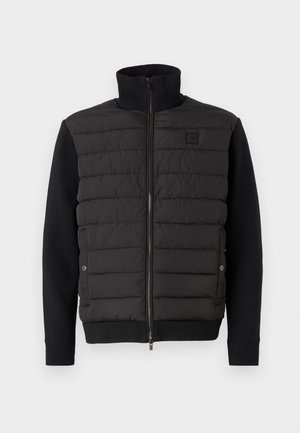 Giacca nera con parte anteriore imbottita, collo alto e polsini a coste. Presenta una chiusura con zip e maniche a contrasto, realizzata con materiali misti.