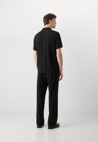 Chemise noire à manches courtes avec un ourlet droit, associée à un pantalon noir ample et des chaussures noires, vue de dos.