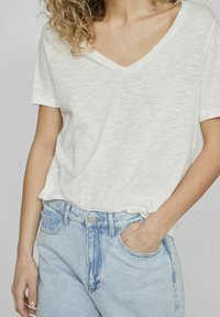 Camiseta blanca de manga corta y escote en V, con una tela ligera y texturizada, combinada con jeans de mezclilla azul claro de alta cintura.