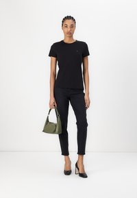 Svart bomulls-t-skjorte, tettsittende design, kombinert med svarte skinny jeans. Tilbehør inkluderer en liten olivengrønn håndveske og svarte hæler.
